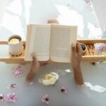 Enjoy a tranquil bath with a book surrounded by flowers and warm tea. Perfect spa day setting.